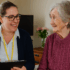 A female occupational therapist in a bright home setting smiles as she speaks with an elderly woman seated comfortably in a chair, reflecting supportive care and community-based therapy.