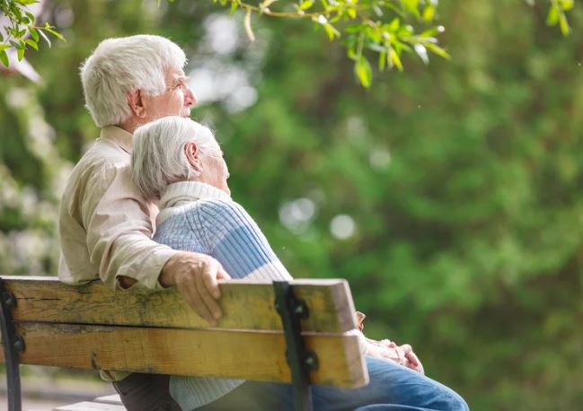 Elderly couple sitting on a park bench on a warm summers day