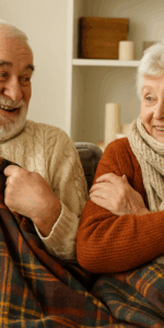 Elderly couple wrapped up on the couch this autumn with blankets, jumpers and scarves