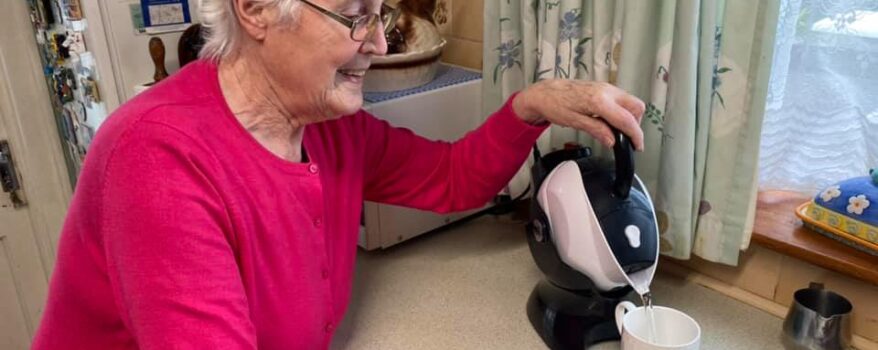 Elderly woman pouring the Uccello Kettle to make a cup of tea in her kitchen